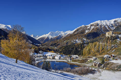 Schloss Tarasp und See in der Nähe von Häusern und schneebedeckten Silvretta Alpen an einem sonnigen Tag, Tarasp, Unterengadin, Engadin, Graubünden, Schweiz - ANSF00798