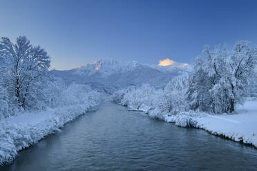 Fluss inmitten von gefrorenen kahlen Bäumen in der Nähe der schneebedeckten bayerischen Alpen, Oberbayern, Bayern, Deutschland - ANSF00810