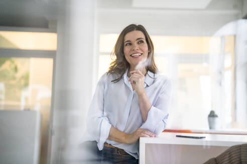 Thoughtful businesswoman leaning on desk in creative office - KNSF10058