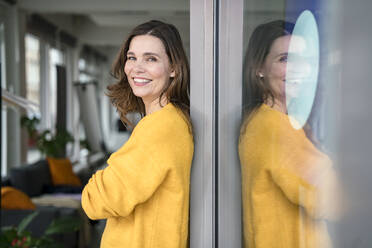 Smiling businesswoman leaning on window in creative office - KNSF10063