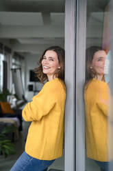Smiling businesswoman leaning on window in office - KNSF10064
