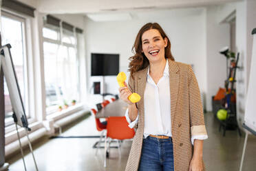 Happy businesswoman holding telephone receiver in creative office - KNSF10070