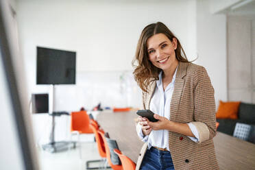 Confident businesswoman with smart phone in meeting room - KNSF10077
