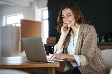 Happy businesswoman working on laptop at desk in office - KNSF10086