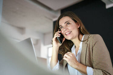 Smiling businesswoman talking on mobile phone in office - KNSF10089