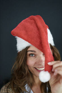 Happy businesswoman in santa hat in front of black background - KNSF10099