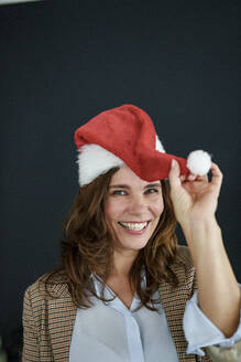 Cheerful businesswoman in santa hat in front of black background - KNSF10100