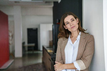 Thoughtful businesswoman leaning on wall in modern office - KNSF10106