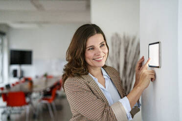 Lächelnde Geschäftsfrau mit moderner Automatisierungstechnik im Büro - KNSF10109
