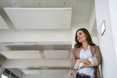 Thoughtful businesswoman leaning by modern automation technology on wall in office - KNSF10116