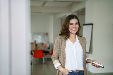 Happy businesswoman holding mobile phone in creative office - KNSF10118