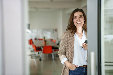 Smiling businesswoman holding smart phone in creative office - KNSF10121