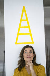 Thoughtful creative businesswoman looking at pyramid sign on wall - KNSF10127