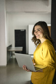 Lächelnde kreative Geschäftsfrau mit Laptop im Büro - KNSF10138