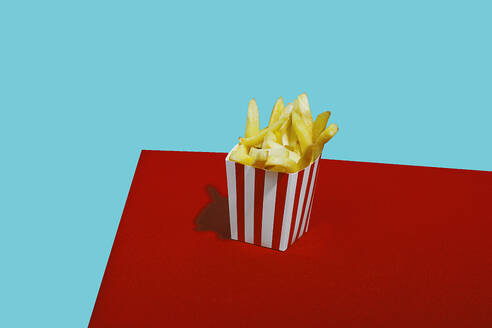 French fries in container on table against blue background - RDTF00060