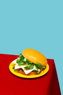 Chicken burger with cheese and lettuce on table against blue background - RDTF00061