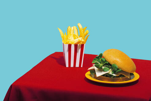 Chicken Burger mit Pommes frites auf Tisch vor blauem Hintergrund - RDTF00063