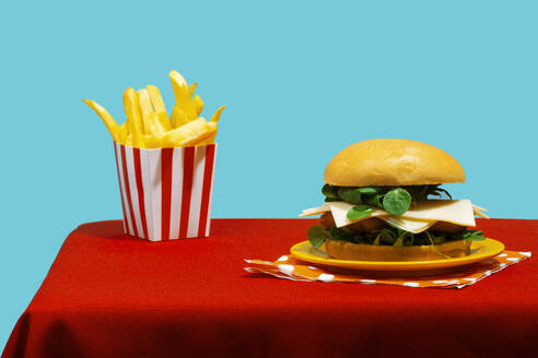 Cheeseburger mit Pommes frites auf Tisch vor blauem Hintergrund - RDTF00064