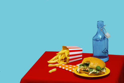 Bite taken from burger near french fries and soda bottle against blue background - RDTF00065