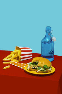 Cheeseburger with french fries near soda bottle on table against blue background - RDTF00066