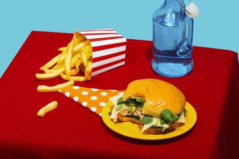 Chicken Burger und Pommes frites mit Soda Flasche auf dem Tisch vor blauem Hintergrund - RDTF00067