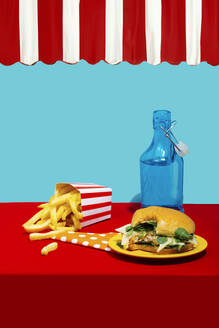 Chicken Burger mit Pommes frites in der Nähe von Soda Flasche auf dem Tisch vor blauem Hintergrund - RDTF00068