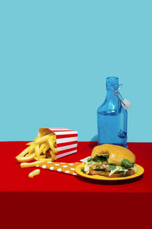 Chicken Burger mit Pommes frites und Soda Flasche auf dem Tisch vor blauem Hintergrund - RDTF00073