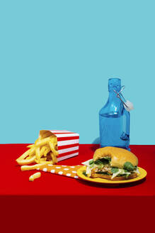 Chicken burger with french fries and soda bottle on table against blue background - RDTF00073