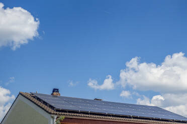 Solar panels on rooftop of house under cloudy blue sky in Bavaria, Germany - MAMF02959