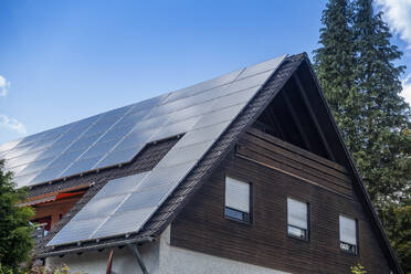 Solar panels on rooftop of house under blue sky in Bavaria, Germany - MAMF02960