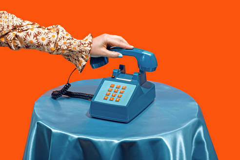 Woman picking up telephone receiver on table against orange background - RDTF00076
