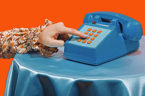 Woman dialing number on telephone against orange background - RDTF00077