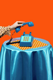 Woman holding telephone receiver on table against orange background - RDTF00078