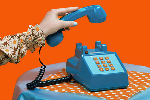 Hand einer Frau, die den Telefonhörer abnimmt, vor orangefarbenem Hintergrund - RDTF00079