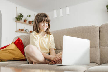 Smiling girl having video call through laptop on sofa at home - ELMF00113