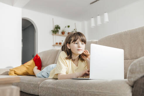 Girl lying down and studying on laptop at home - ELMF00114