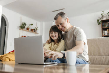 Happy father and daughter watching movie on laptop at home - ELMF00115