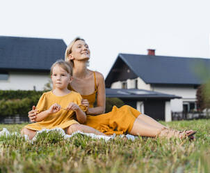 Smiling mother sitting with daughter on grass in meadow - NDEF01606