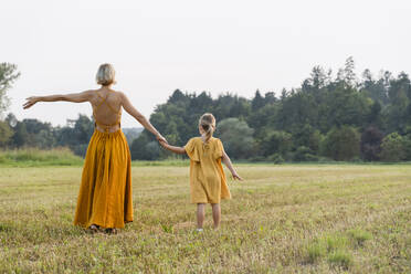 Mother holding hand of daughter and walking in meadow - NDEF01609