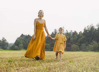 Mother and daughter holding hands and walking in meadow - NDEF01610