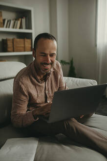 Smiling freelancer talking on video conference through laptop at home office - DMGF01286