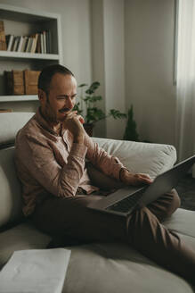 Freelancer sitting on sofa and having video conference at home office - DMGF01287