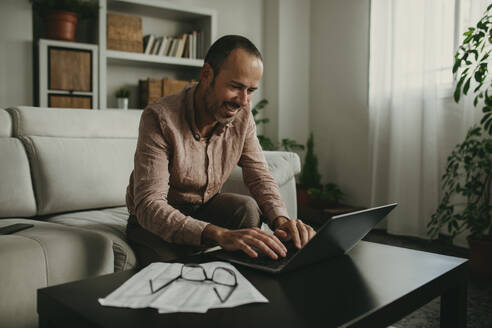 Smiling freelancer working on laptop at home office - DMGF01289