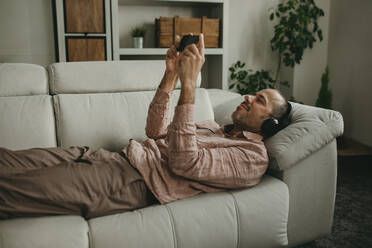 Man lying down and watching movie on smart phone at home - DMGF01302