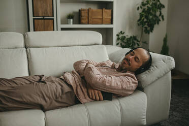 Mann hört Musik und entspannt sich auf dem Sofa zu Hause - DMGF01303
