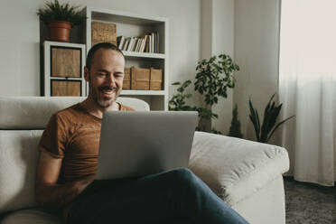 Happy man watching movie on laptop at home - DMGF01304