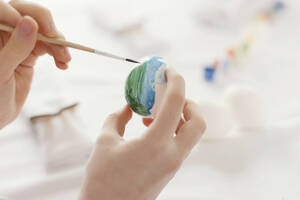 Hands of girl painting Easter egg using brush at home - ONAF00731