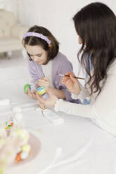 Woman teaching daughter to paint Easter eggs at home - ONAF00734