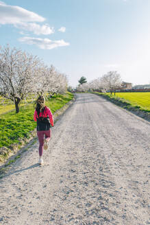 Frau läuft auf unbefestigtem Weg inmitten einer Wiese an einem sonnigen Tag - EGHF00884