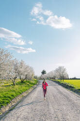 Frau läuft auf unbefestigtem Weg inmitten von Mandelblüten an einem sonnigen Tag - EGHF00885